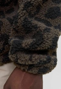 Bruin en zwart gemarmerde fleece-stof met een zachte, gestructureerde oppervlakte, met een opgerolde manchette en natuurlijke, aardse tinten.