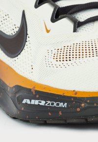 Athletic shoe featuring a white mesh upper, orange and black accents, textured sole, and “AIR ZOOM” branding with splattered details.
