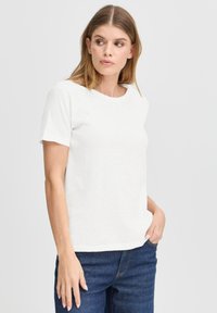 T-shirt bianco a maniche corte realizzato in tessuto testurizzato, con scollatura rotonda e vestibilità comoda, abbinato a jeans blu scuro.