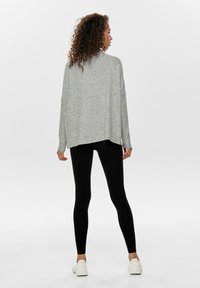 Un pull surdimensionné gris clair avec une coupe décontractée, associé à des leggings noirs et des baskets blanches, vu de dos pour mettre en valeur le design et la couleur.