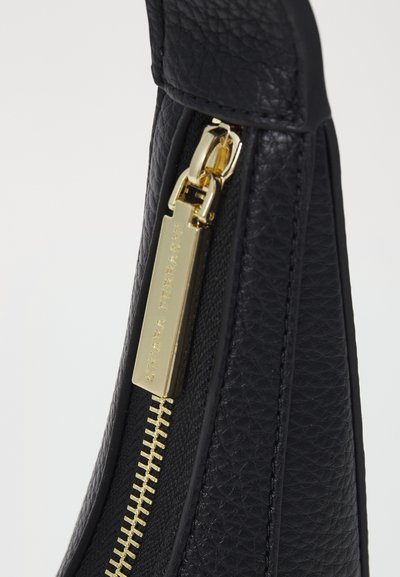 Μαύρη δερμάτινη τσάντα με υφασμάτινη επιφάνεια, που διαθέτει χρυσό φερμουάρ και λαβή. Το φερμουάρ εκτείνεται κατά μήκος της άνω πλευράς με λεπτομερή ραφή.