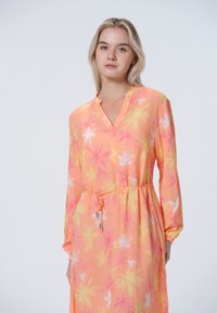 Langärmliges, V-Ausschnitt-Kleid in Pfirsich mit floralen Mustern in Pink und Gelb. Verstellbare Taillendetails und leichter, fließender Stoff.