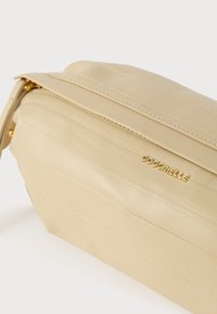 Beežist nahast käekott pehme tekstuuriga, kuldse luku ja esiküljel kuldse "Coccinelle" logoga.