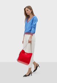 Ljusblå V-ringad tröja med röda och vita ränder, vita vida byxor och en texturerad röd handväska med en logotyp. Svarta spetsiga slingbacks.