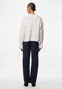 Πλεκτό πουλόβερ στο χρώμα της κρέμας με χαμηλωμένους ώμους, φαρδύ ντεκολτέ και ριμπ τελείωμα, σε συνδυασμό με σκούρο μπλε τζιν παντελόνι με φαρδιές μπλούζες.