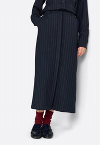 Gonna a righe navy realizzata in tessuto dalla trama liscia, con uno spacco frontale e una vita alta, abbinata a scarpe scure e calzini rossi.