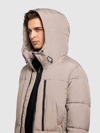 Prešívaná bunda v svetlobéžovej farbe s veľkou kapucňou, zipsovou náprsnou vreckom a prednými vreckami. Hladká textúra a viditeľný prešívaný vzor.