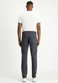 Pantalones grises de corte recto, fabricados en una tela suave. Cuentan con cinturilla, presillas para el cinturón y dos bolsillos traseros. Camiseta blanca visible.