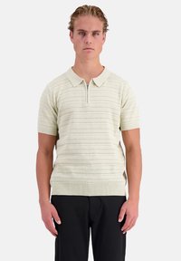 Korte mouwen pullover in lichtgroene brei met gestructureerde horizontale strepen, een ritskraag en een geribbelde zoom. Gestyled met zwarte broeken.