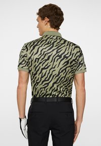 Grön polo skjorta med ett svart tigerrandigt mönster, korta ärmar och krage. Bärs med svarta byxor och ett svart bälte. Vit handske på handen.