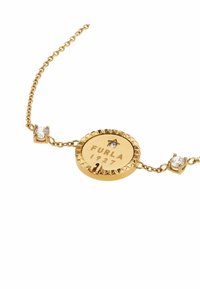Pulsera en tono dorado con un charm redondo de borde texturizado, grabado "FURLA 1927", y acentuada por dos pequeñas piedras preciosas transparentes.