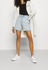 Shorts en denim bleu clair à taille haute, dotés de cinq poches et d'un ourlet brut, associés à un haut noir et des sneakers blanches.