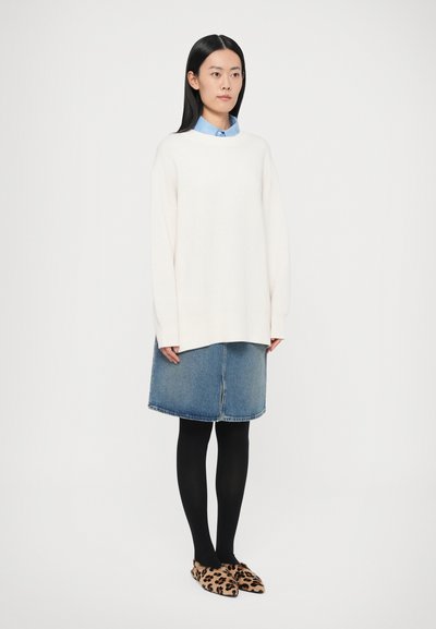 Túlméretezett krémszínű pulóver, világoskék galléros ing alatta, farmer A-vonalú szoknya, fekete harisnya és leopárdmintás bebújós cipők.