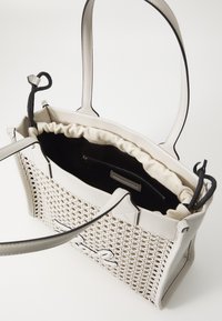 Didelis rankinys su nupinta išore, off-white spalvos, su lygiais odiniais akcentais. Vidinė pamušalas yra minkštas smėlio spalvos audinys su užtrauktuku.