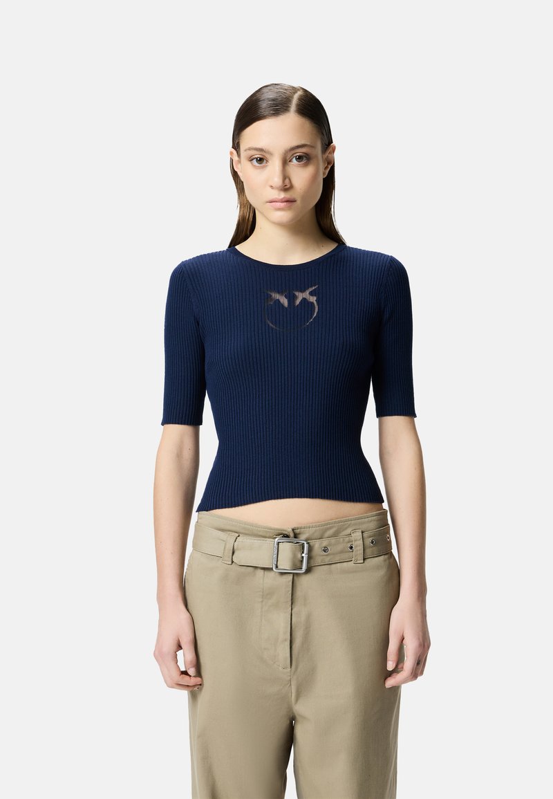 Top corto a coste blu navy con maniche corte, caratterizzato da un design con aperture sul petto. Abbinato a pantaloni beige chiaro a vita alta e cintura.