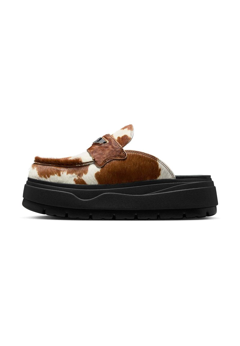 Brun og hvid ko-print slip-on sko med tyk sort plattformsål og et dekorativt sort metalemblem på overdelen.