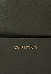 Temnozeleni usnjeni nahrbtnik z teksturirano površino. Ima zlati logotip "VALENTINO", minimalistični design in eleganten oblik.