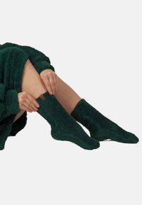 Calze verdi e pelose con una texture morbida. Lunghezza a metà polpaccio, con un piccolo etichetta marrone al polsino. Materiale soffice per il calore.