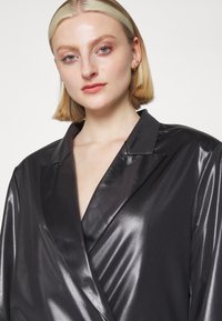 Mustrite satin bleiser, millel on šaalikaelus, sujuva tekstuuri, kerge sära ja kohandatud lõige, rõhutades kaasaegset disaini.