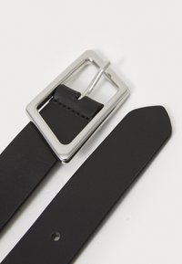 Cinturón de cuero negro con una hebilla rectangular plateada. La correa es lisa, con un agujero para ajuste y con un extremo redondeado.