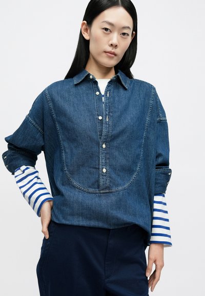 Πουκάμισο από τζιν με ραφή κυρτού γιοκ και μανίκια με μπλε και λευκές ρίγες, διαθέτει κλασικό γιακά και ασημένια κουμπιά.