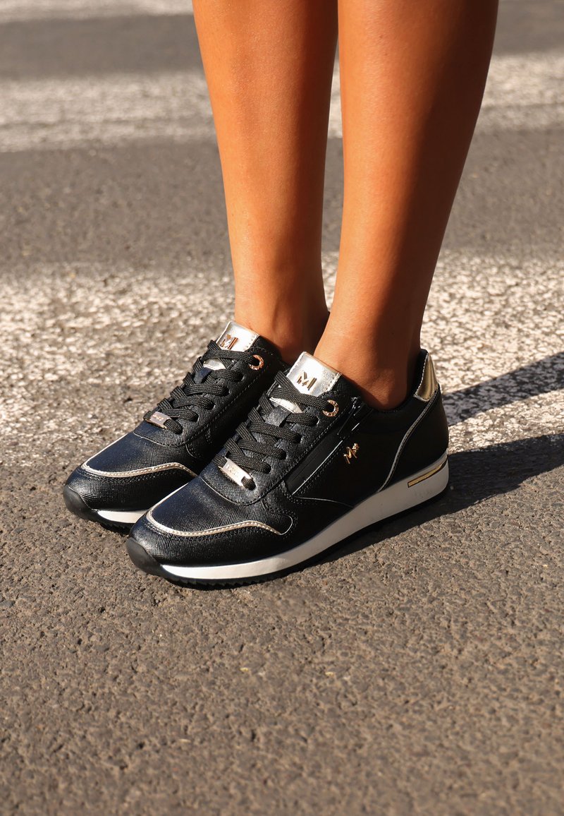 Czarne sneakersy o teksturowanym wykończeniu, złote akcenty na języku i pięcie, biała gumowa podeszwa oraz czarne sznurówki. Widoczne kontrastowe przeszycia.