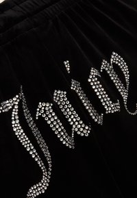 Tissu noir avec ceinture élastique, orné du texte « smile » et d'un symbole de cœur composé de petits strass argentés brillants.