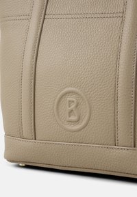 Borsa a mano in pelle beige con finitura testurizzata, caratterizzata da cuciture pronunciate e un logo embossato circolare sulla parte anteriore.