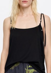 Black sleeveless top made of soft fabric, featuring a straight neckline and adjustable strap with silver hardware detail on the left side.