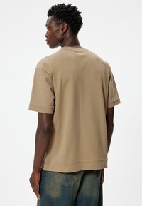 Beige katoenen t-shirt met korte mouwen en een ontspannen pasvorm, voorzien van een ronde halslijn en een iets langere achterkant.
