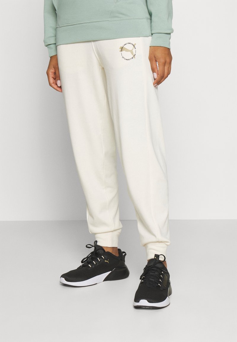 Light green sweatshirt with a kangaroo pocket, paired with cream sweatpants featuring a printed logo. Black athletic shoes with white soles.