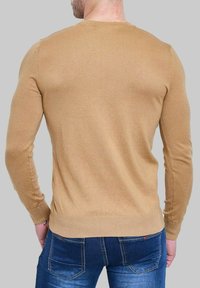 Pull en tricot beige avec des manches longues et un col rond, texture lisse, coupe ajustée, couture visible et détail de bord-côte.