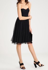 Svart strapless klänning med en åtsittande kropp, svängande kjol och tyllöverdrag. Matchas med svarta högklackade sandaler med remmar.