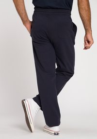 Pantaloni blu navy con elastico in vita, una tasca posteriore, design con gamba affusolata e texture liscia, abbinati a sneakers alte bianche.