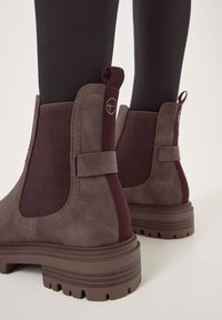 Stivali ankle in pelle marrone con pannelli laterali elastici bordeaux, finitura in suede testurizzato e suole in gomma spesse. Presentano un cinturino di trazione e un dettaglio del logo.