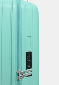 Valigia rigida di colore verde menta. Presenta una superficie texturizzata, doppie zip e una serratura a combinazione con un buco per la chiave.