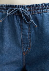 Blauwe denim joggers met een elastische tailleband, trekkoord en oranje stiksels. Heeft een gladde textuur en zijzakdetails.