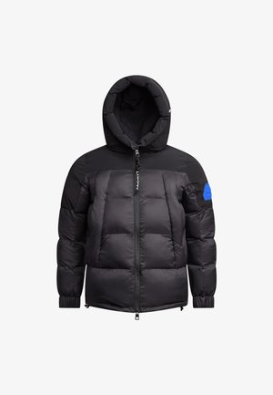 Giacca piumino nera con cappuccio, caratterizzata da un design trapuntato, chiusura con zip, polsini a coste e una toppa accentuata di colore blu sulla spalla sinistra.