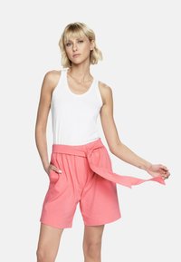 Różowe bawełniane szorty z wiązanym paskiem w talii, bocznymi kieszeniami i luźnym krojem, zestawione z białym topem na ramiączkach. Gładka tekstura i swobodny styl.