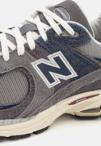 Šedé a námořnické tenisky New Balance s prodyšnou a texturovanou semišovou vrstvou, výrazným logem "N" a polstrovanou podrážkou s červeným akcentem.