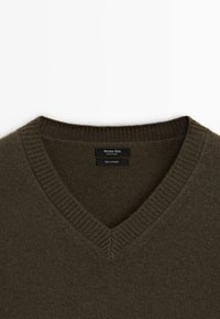 Maglione in cashmere verde oliva scuro con scollo a V, colletto a coste e etichetta che mostra dettagli del marchio e del materiale.