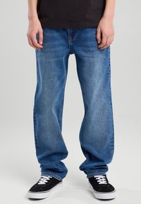 Siniset farkut, joissa on löysä istuvuus, viisi taskua ja hienovarainen kuluminen. Yhdistetty mustiin tennareihin, joissa on valkoiset nauhat ja klassinen muotoilu.