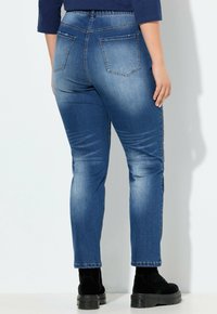 Jeans de mezclilla azul con un corte ajustado, que cuentan con una cintura alta y bolsillos traseros. La tela presenta un ligero efecto de desvanecimiento y un sutil desgaste.