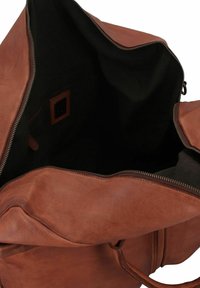 Sac en cuir marron avec une fermeture éclair, offrant un intérieur spacieux doublé de tissu noir et une petite étiquette en cuir à l'intérieur.