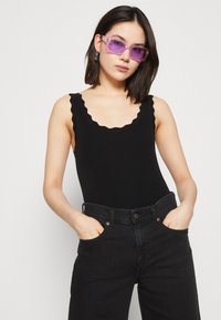 Sort ribbet bodysuit med bølget udkant, parret med højtaljede sorte jeans. Model iført transparente lilla solbriller.