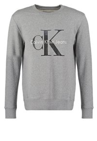 Sweatshirt gris à manches longues avec des poignets et un ourlet côtelés, présentant un grand logo en texte "cK" et "Calvin Klein Jeans" sur le devant.