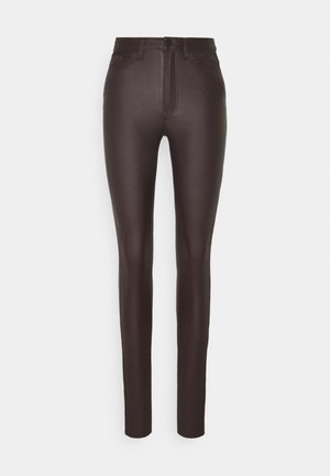 Ciemnobrązowe, dopasowane spodnie z przednim zapięciem na guzik i zamek, szlufkami na pasek oraz przednimi kieszeniami na jednolitym białym tle.