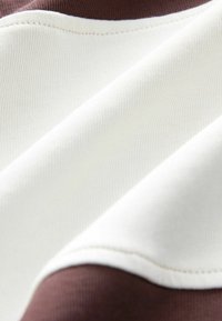 Stoffmuster in Creme- und Brauntönen, glatte Textur und leichter Glanz. Sichtbare Nähte entlang der Kanten.