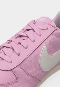 Gros plan sur une basket en cuir rose avec des lacets assortis et un logo Nike swoosh blanc sur le côté.
