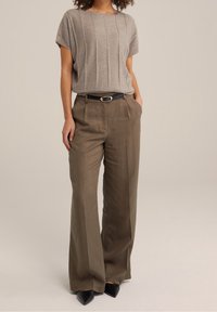 Ljusgrå stickad topp med korta ärmar och vertikala ränder, parat med hög midja olivgröna vida byxor, svart bälte och spetsiga klackar.